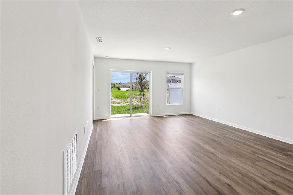 An empty room with wood-look flooring, white walls, recessed lighting, and a sliding glass door — 1134 AMBER WAVES COURT, LAKE WALES, FL