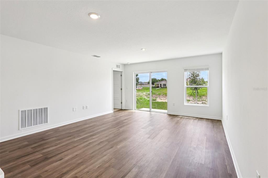 An empty room with white walls, wood-look flooring, a sliding glass door, and one window — 1134 AMBER WAVES COURT, LAKE WALES, FL