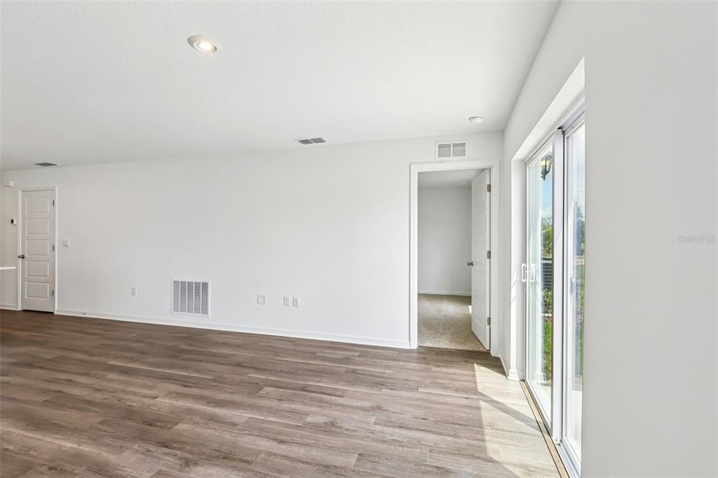 An empty room with white walls, wood-look flooring, a doorway, and sliding glass doors — 1134 AMBER WAVES COURT, LAKE WALES, FL
