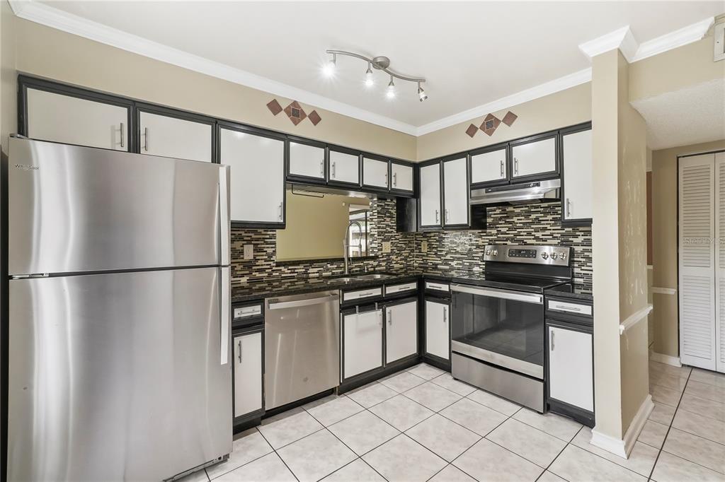 A kitchen with stainless steel appliances, dark-trimmed white cabinets, and a mosaic tile backsplash — 5002 CORVETTE DRIVE, TAMPA, FL