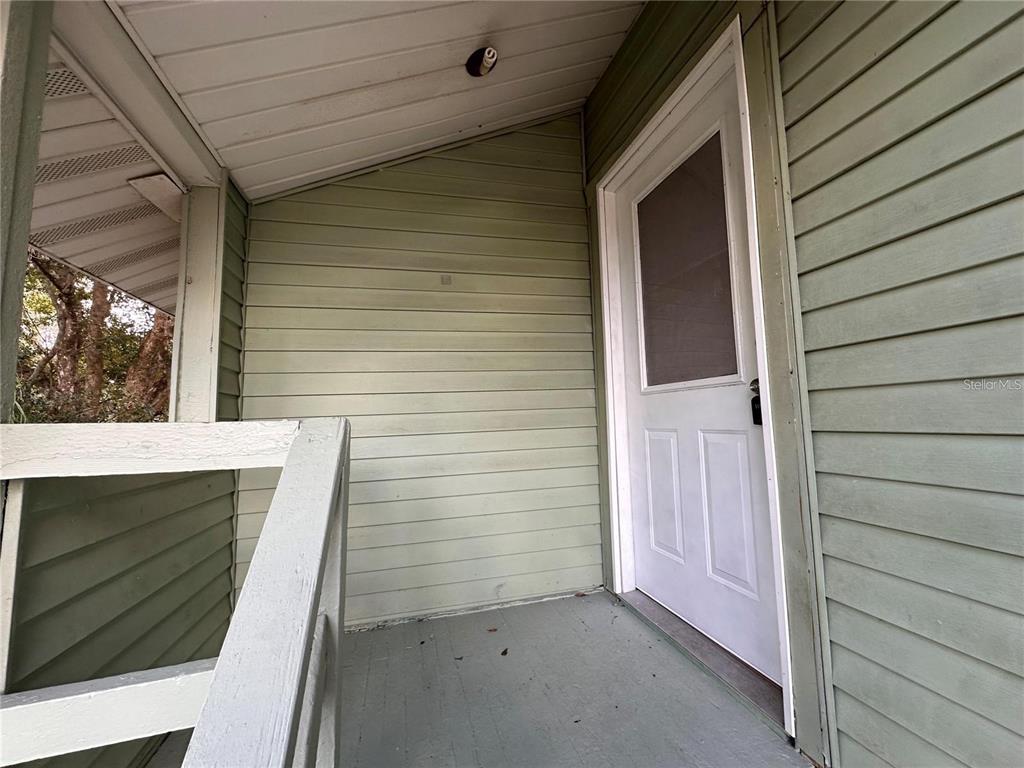 A covered porch features light green horizontal siding, a white door, and a wooden railing — 1025 E MAIN STREET, BARTOW, FL