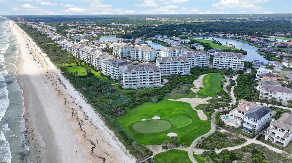 An aerial view shows beachfront condominiums, a golf course green, and surrounding residential homes — 300 CINNAMON BEACH WAY UNIT 221, PALM COAST, FL