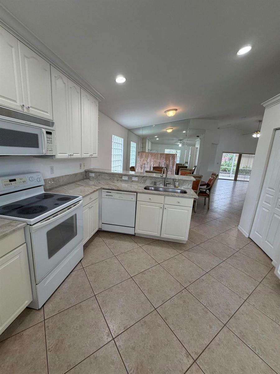 A bright, empty living room features beige tile flooring, a ceiling fan, and sliding glass doors — 8046 Florenza Drive, Boynton Beach FL 33472, BOYNTON BEACH, FL
