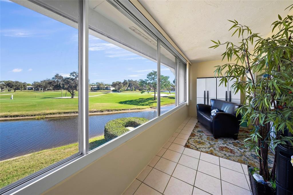 A sunroom with tile flooring, a black sofa, and large windows overlooking a golf course — 7193 W COUNTRY CLUB DRIVE N UNIT 237, SARASOTA, FL