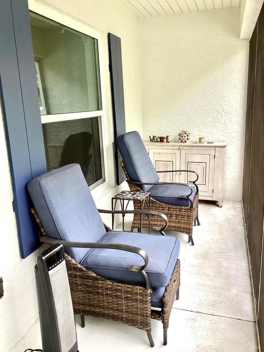 A covered patio features two wicker chairs with blue cushions and a small wooden cabinet — 23 Highlands Drive SW, Vero Beach FL 32962, VERO BEACH, FL