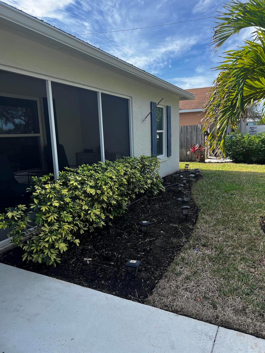 A side view of a house features a screened-in porch, landscaping, and outdoor path lighting — 23 Highlands Drive SW, Vero Beach FL 32962, VERO BEACH, FL