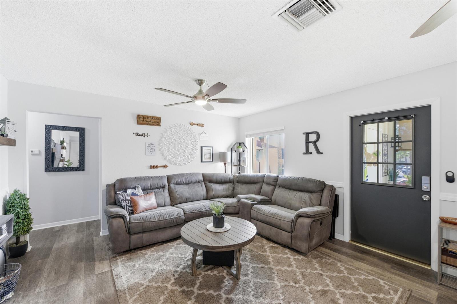 A living room features a grey sectional sofa, a round wooden coffee table, and a door — 5883 La Paseos Drive # 2, FL 33463, FL