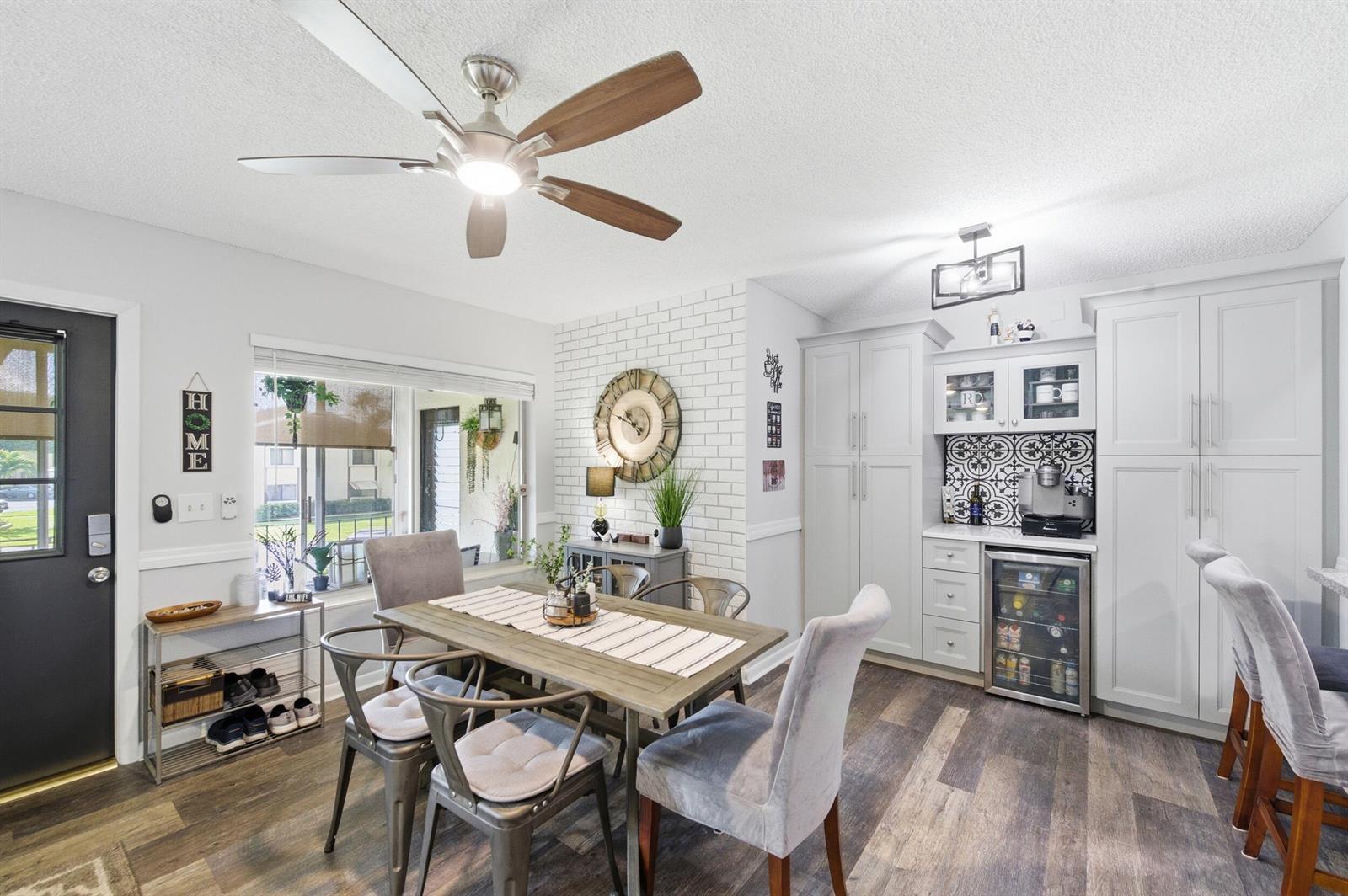 A dining area features a wooden table, grey chairs, a brick accent wall, and cabinetry — 5883 La Paseos Drive # 2, FL 33463, FL
