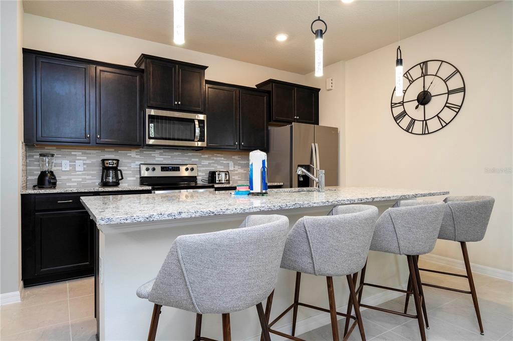 A kitchen features dark cabinets, granite countertops, a central island with four chairs, and stainless appliances — 4458 KAIPO ROAD, DAVENPORT, FL