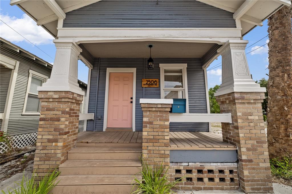 A front porch with brick pillars, a pink door, and gray siding on a house — 2506 1/2 E COLUMBUS DRIVE, TAMPA, FL