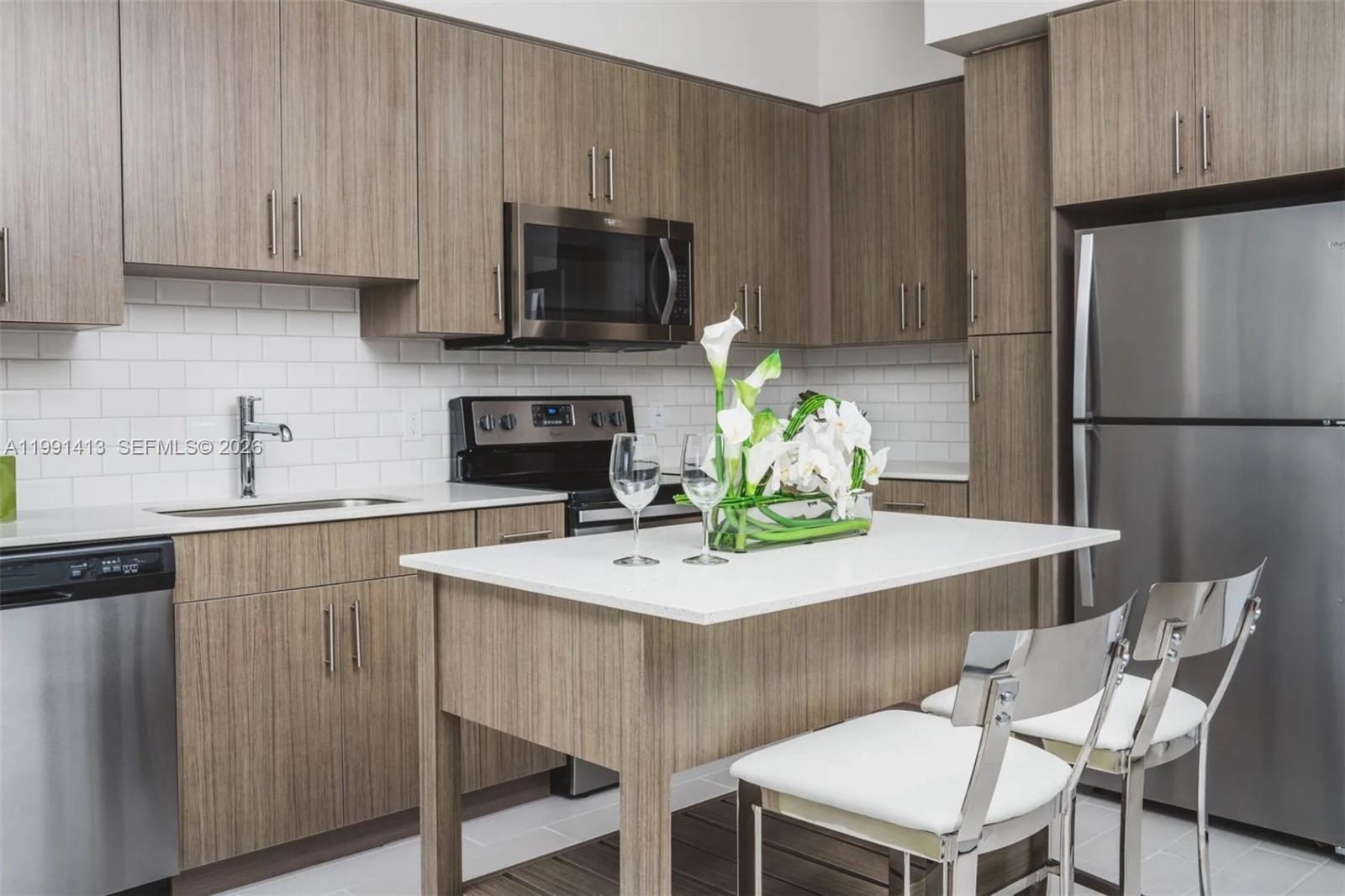 A modern kitchen features wood-grain cabinets, stainless steel appliances, white countertops, and a central island — 1170 NW 11th St # 119, Miami FL 33136, MIAMI, FL
