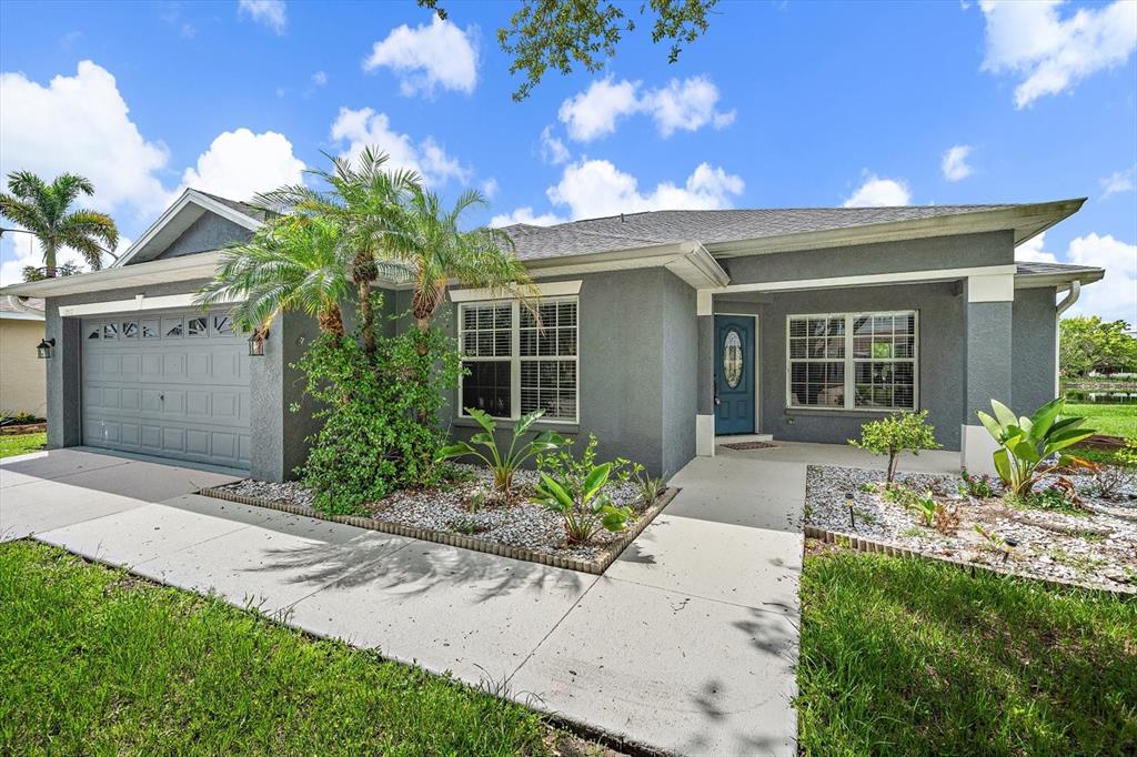 A gray single-story house features a two-car garage, a blue front door, and landscaping — 12017 LARSON LANE, PARRISH, FL