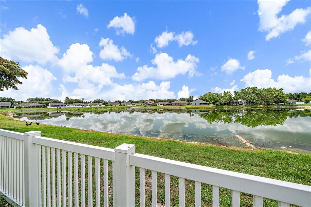 A white fence overlooks a pond with houses in the background under a blue sky — 12017 LARSON LANE, PARRISH, FL