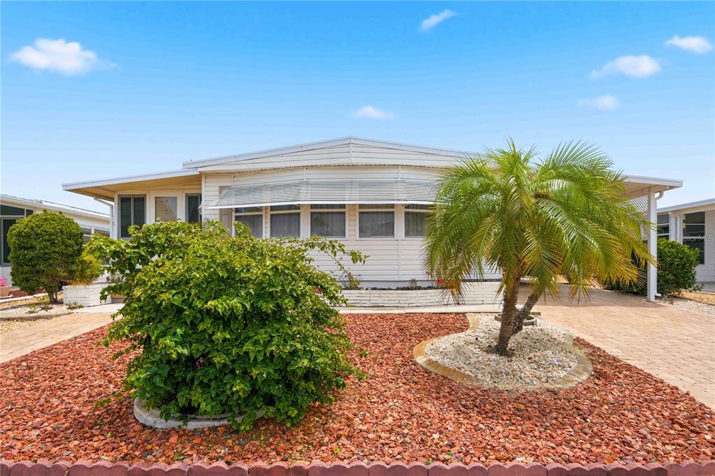 A single-story manufactured home with white siding, a palm tree, and red gravel landscaping — 16 S GRANADA PLAZA, ENGLEWOOD, FL