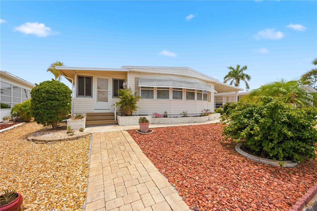 A single-story manufactured home features light siding, a paved walkway, and red gravel landscaping — 16 S GRANADA PLAZA, ENGLEWOOD, FL