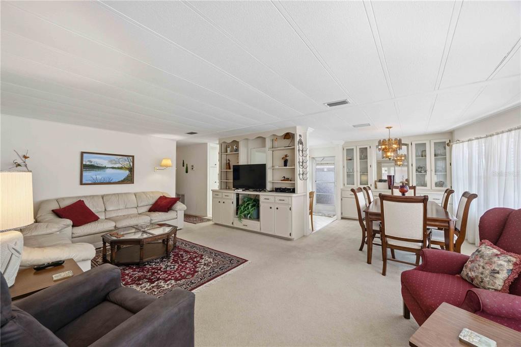 A living and dining room with white walls, beige carpet, and a built-in media center — 16 S GRANADA PLAZA, ENGLEWOOD, FL
