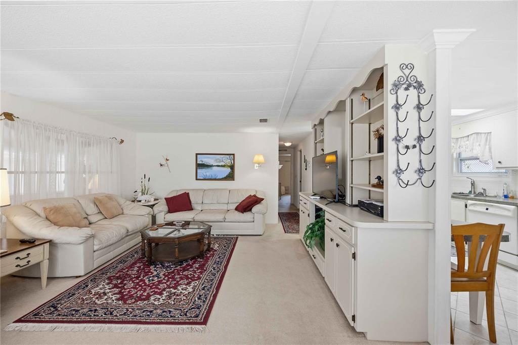 A living room with white walls, beige carpet, a red area rug, and built-in shelving — 16 S GRANADA PLAZA, ENGLEWOOD, FL