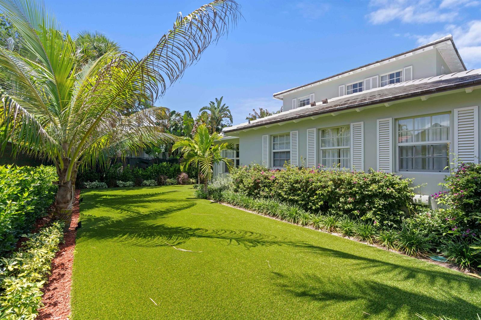 A backyard with artificial turf, lush landscaping, and a light green house with white shutters — 1554 N Ocean Way, Palm Beach FL 33480, PALM BEACH, FL