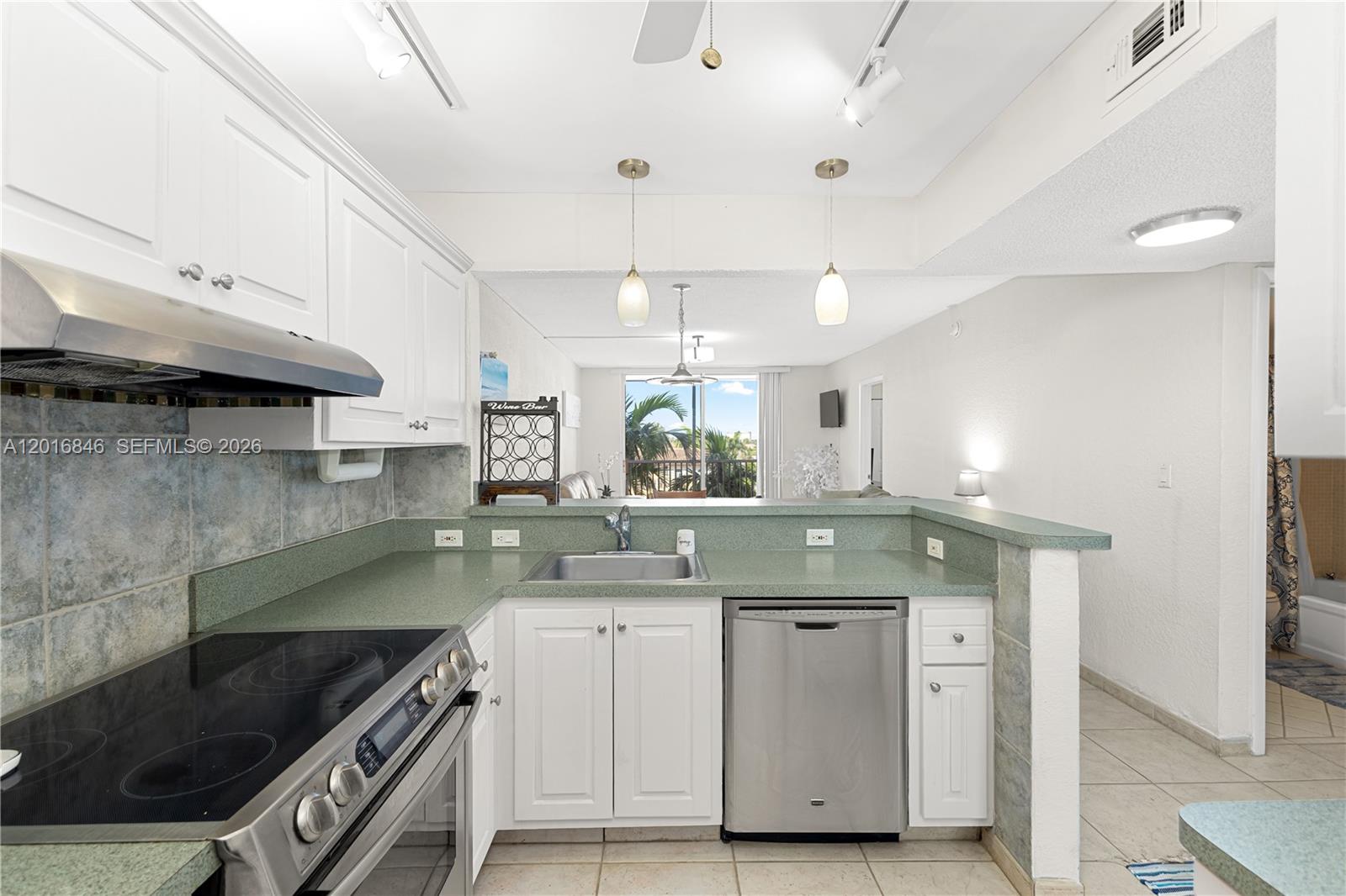 A kitchen with white cabinets, green countertops, and stainless steel appliances overlooks a living area — 1391 S Ocean Blvd # 409, Pompano Beach FL 33062, POMPANO BEACH, FL