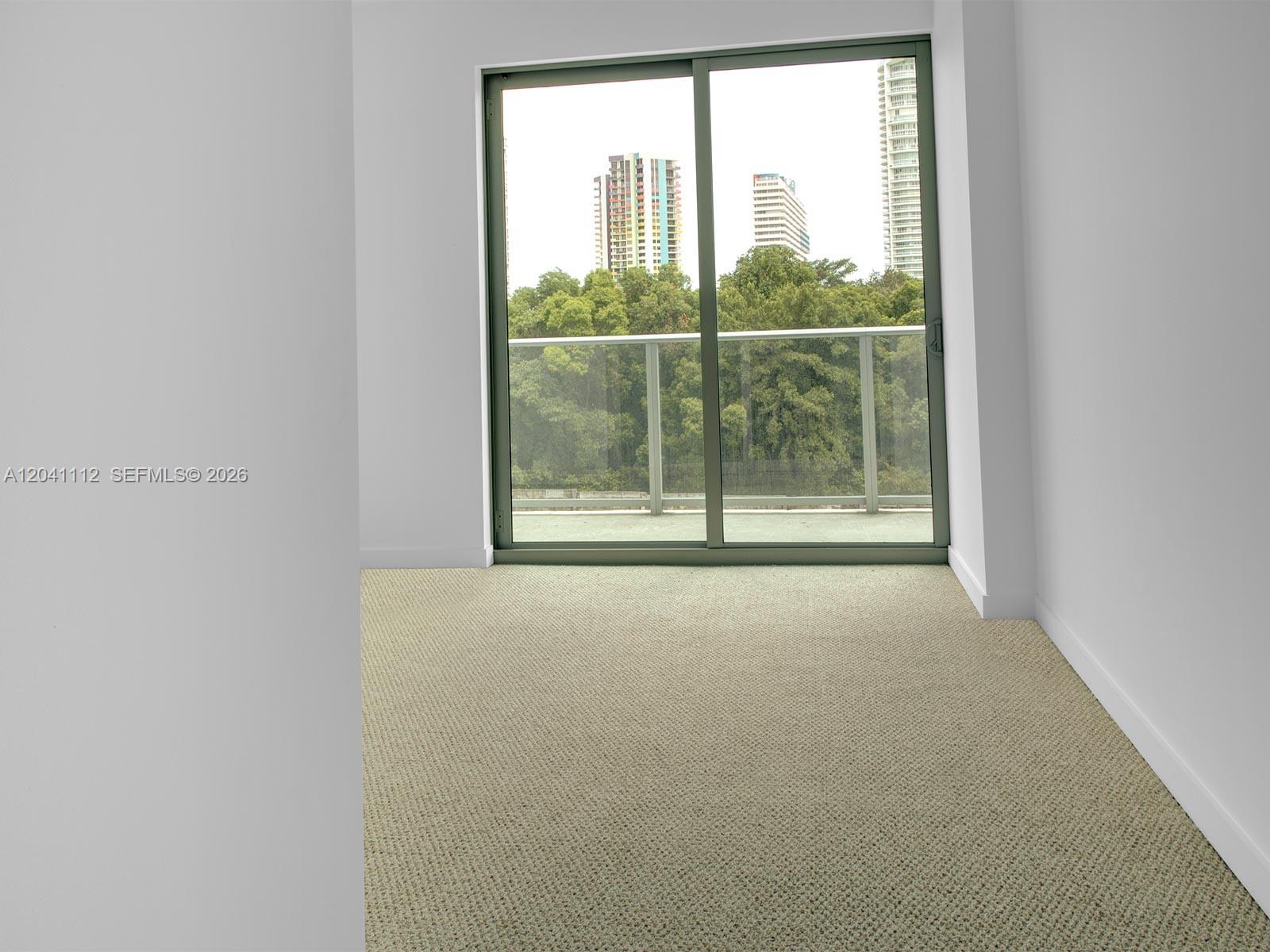 An empty room features beige carpeting, white walls, and a sliding glass door to a balcony — 1600 SW 1st Ave # 401, Miami FL 33129, MIAMI, FL