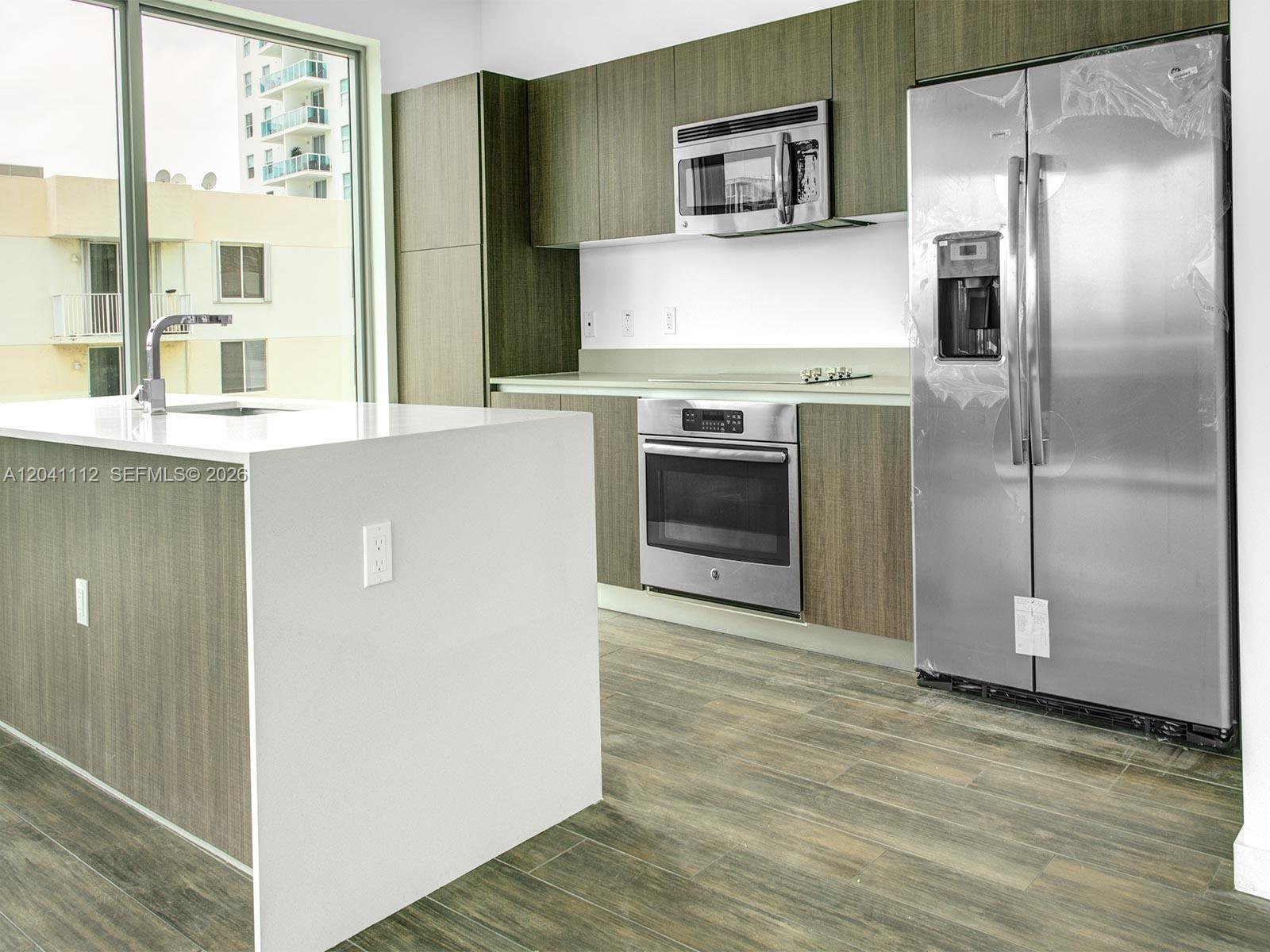 A modern kitchen features wood-grain cabinetry, stainless steel appliances, and a white waterfall island — 1600 SW 1st Ave # 401, Miami FL 33129, MIAMI, FL