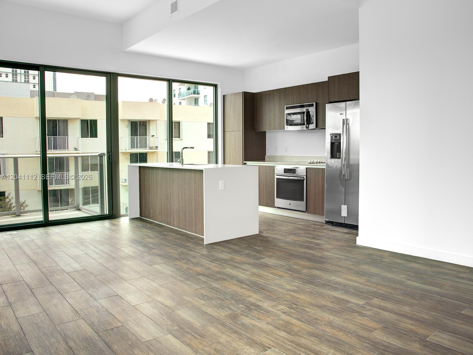 A modern kitchen features wood-tone cabinetry, stainless steel appliances, and a white island with a sink — 1600 SW 1st Ave # 401, Miami FL 33129, MIAMI, FL