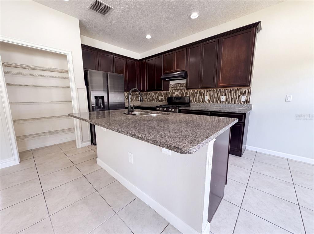A kitchen features dark wood cabinets, granite countertops, a center island, and a walk-in pantry — 881 HARING LANE, MOUNT DORA, FL