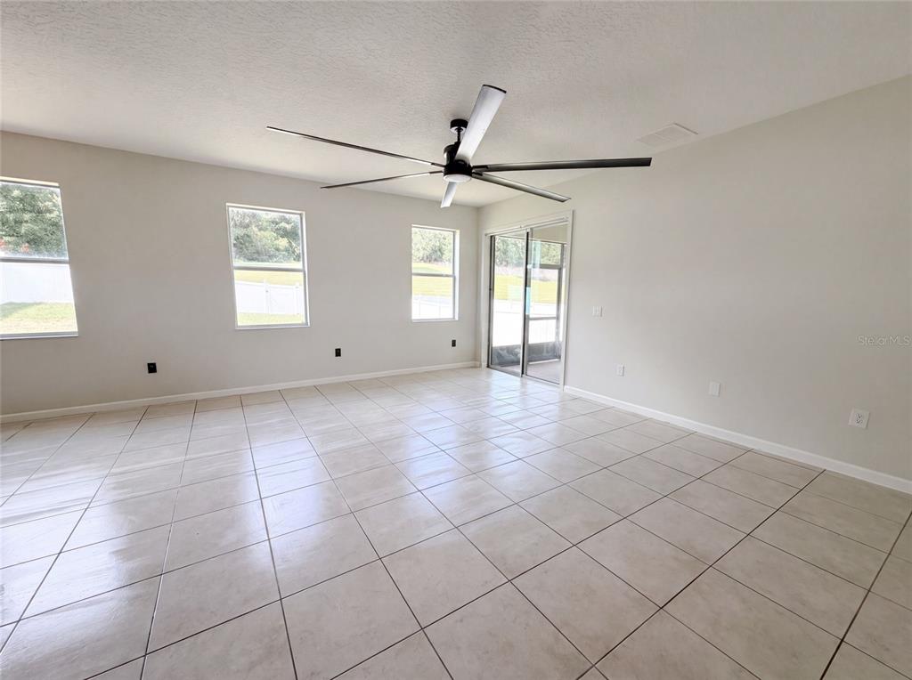 An empty room features light-colored tile flooring, neutral walls, a ceiling fan, and sliding glass doors — 881 HARING LANE, MOUNT DORA, FL