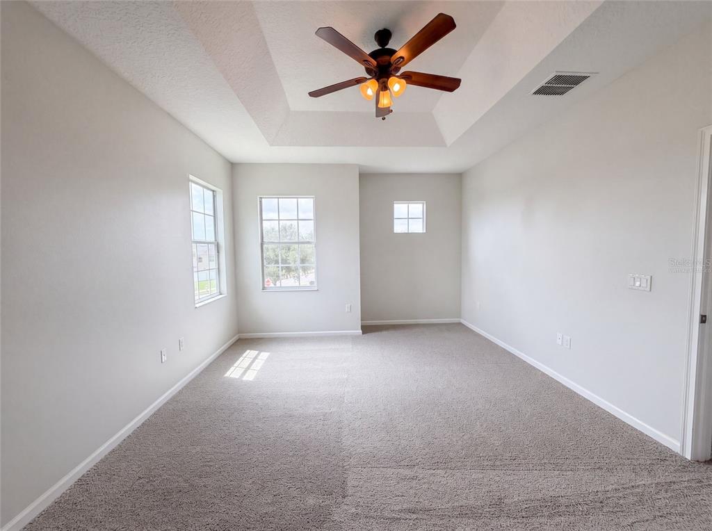 An empty bedroom with gray carpet, white walls, a tray ceiling, and a ceiling fan — 881 HARING LANE, MOUNT DORA, FL