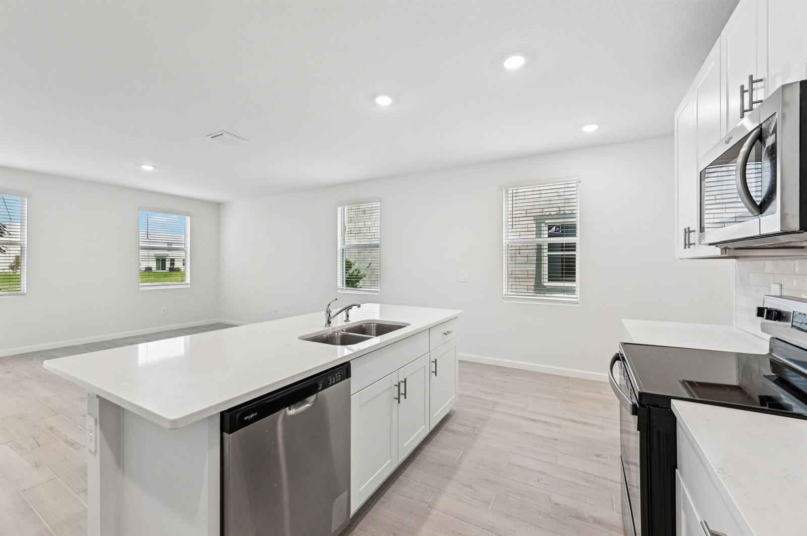 An open-concept kitchen and living area features white cabinetry, stainless steel appliances, and light-colored flooring — 608 Salisbury Circle, Fort Pierce FL 34982, FORT PIERCE, FL