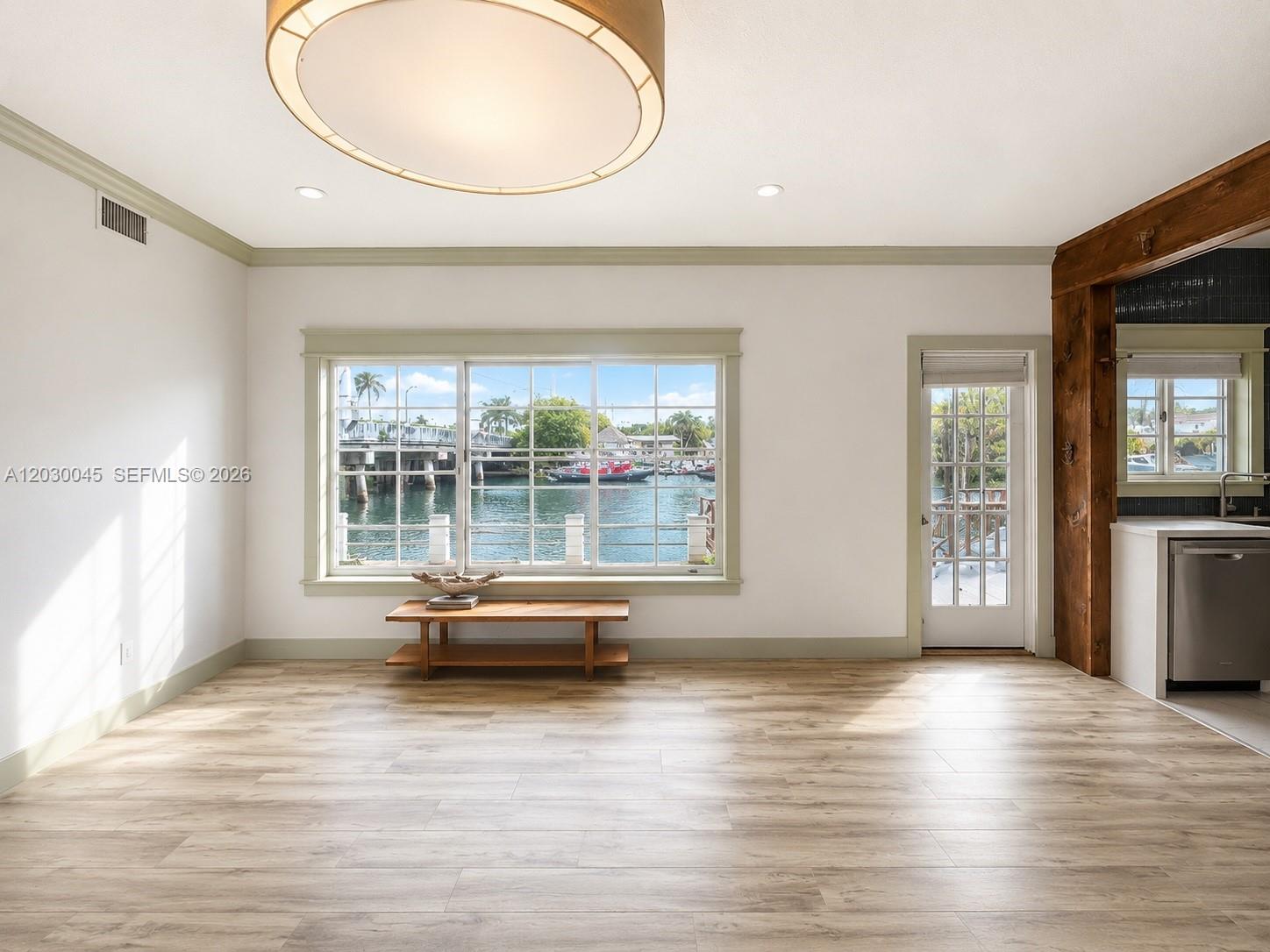 A bright room with wood-look flooring, a large window overlooking a canal, and a door — 2137 Calais Dr # 5, Miami Beach FL 33141, MIAMI BEACH, FL