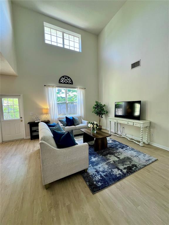 A living room with high ceilings, light wood flooring, a sofa, and a television console — 411 DURHAM SHORE COURT, APOLLO BEACH, FL