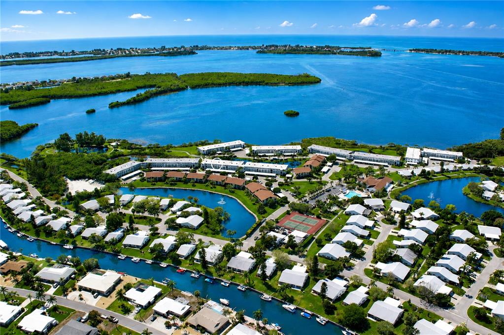 An aerial view shows a waterfront residential community with canals, swimming pools, and tennis courts — 4809 INDEPENDENCE DRIVE, BRADENTON, FL