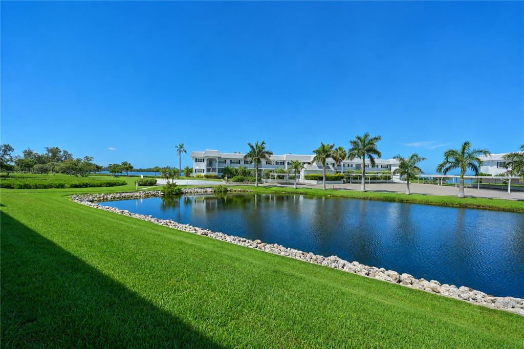 A pond sits in front of a multi-story apartment building with palm trees and parking — 4809 INDEPENDENCE DRIVE, BRADENTON, FL
