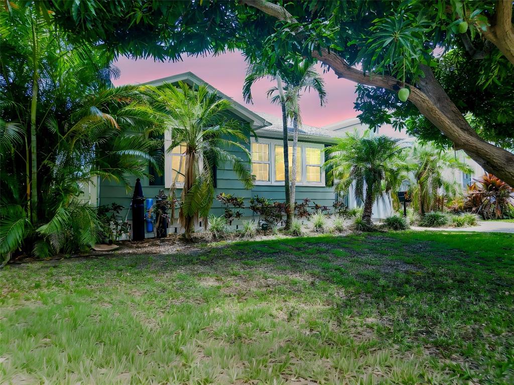 A green house with white-trimmed windows is surrounded by lush tropical trees and landscaping — 182 29TH AVENUE N, ST PETERSBURG, FL