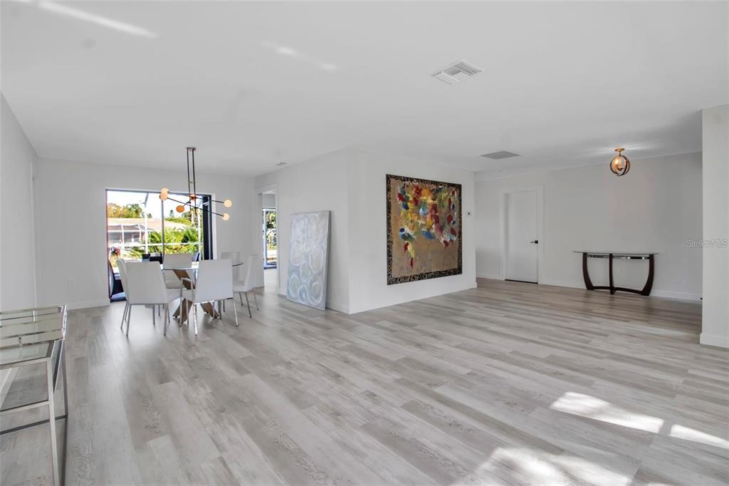 A bright dining and living area features light wood-look flooring, white walls, and modern decor — 1649 STANFORD LANE, SARASOTA, FL