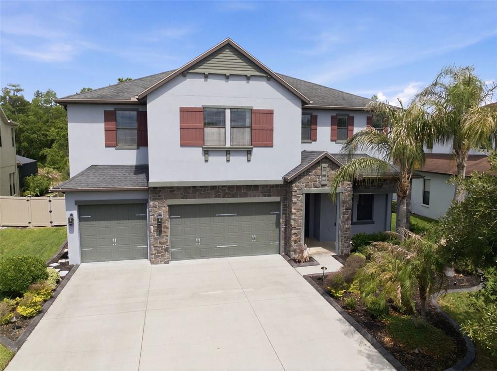 A two-story suburban house with a three-car garage, stone accents, and a concrete driveway — 4335 ORTONA LANE, WESLEY CHAPEL, FL