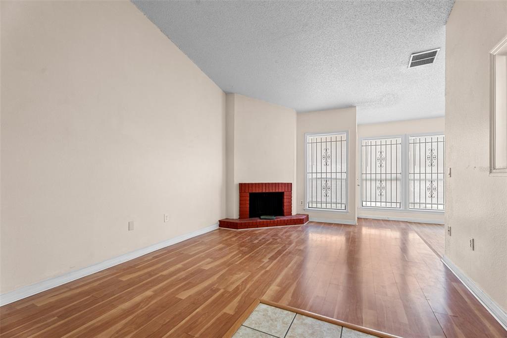 A living room with wood-look flooring, a corner red brick fireplace, and windows with bars — 652 SAINT JHONS UNIT 652, WINTER PARK, FL