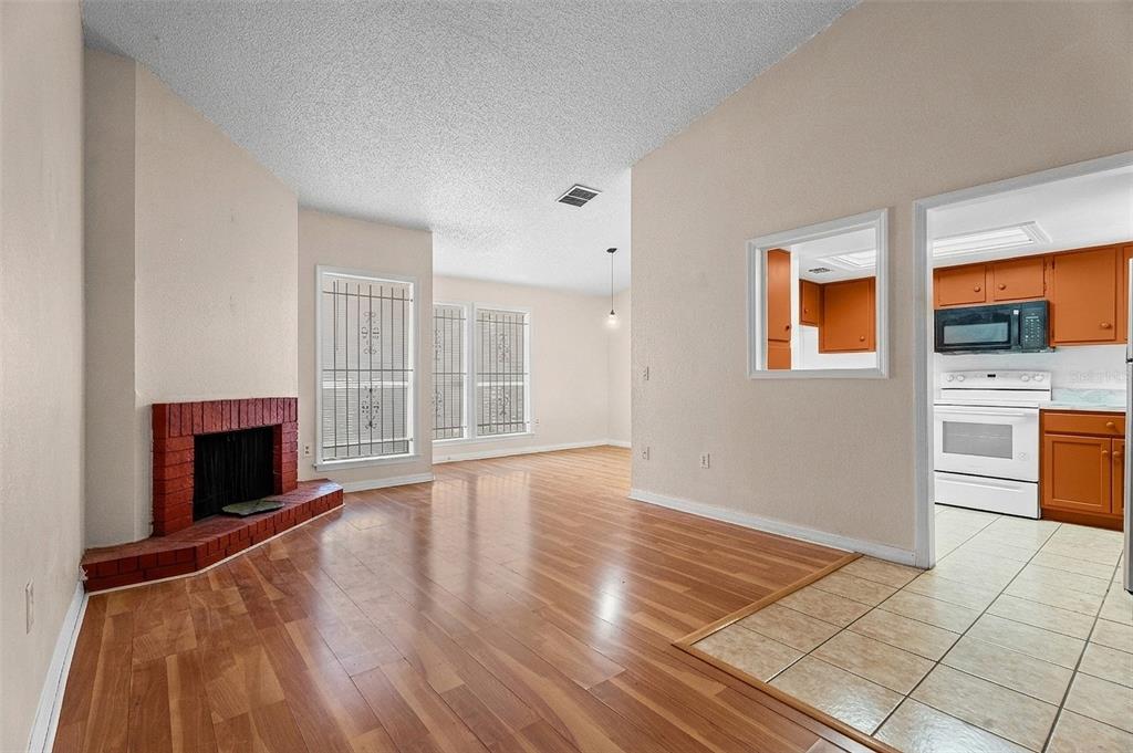 A living room with wood flooring, a red brick fireplace, and an adjacent kitchen — 652 SAINT JHONS UNIT 652, WINTER PARK, FL