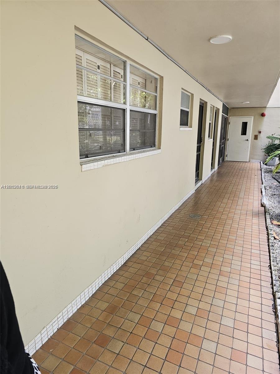 An exterior walkway features tan tiled flooring and a long wall with windows and doors — 1670 NE 191st St # 3, Miami FL 33179, MIAMI, FL