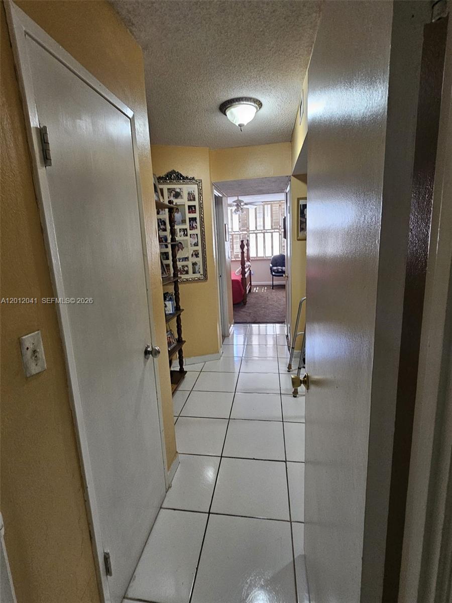 A tiled hallway leads to a bedroom with a view of a windowed sunroom — 1670 NE 191st St # 3, Miami FL 33179, MIAMI, FL