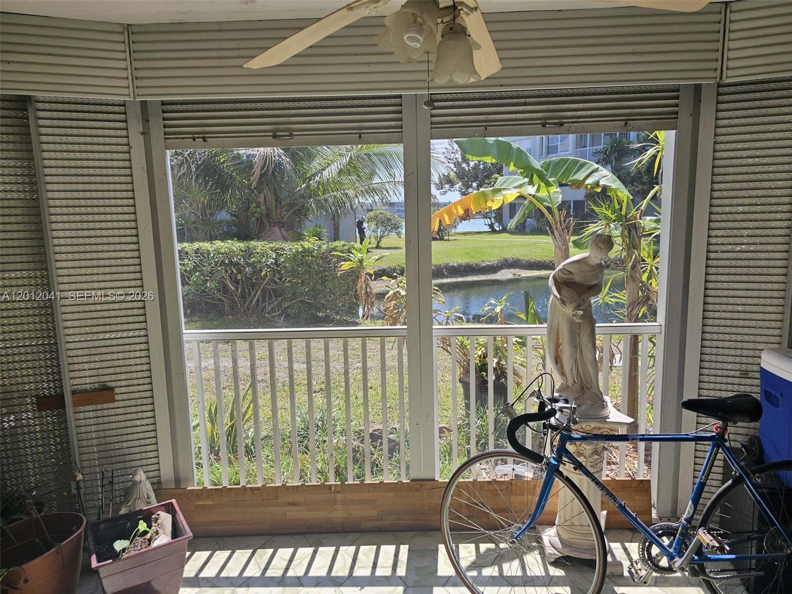 A screened-in porch features a bicycle, a statue, and a view of a pond — 1670 NE 191st St # 3, Miami FL 33179, MIAMI, FL