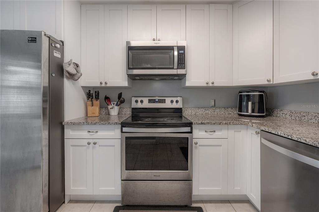 A kitchen features white cabinets, stainless steel appliances, and speckled granite countertops — 5937 13TH AVENUE N, ST PETERSBURG, FL
