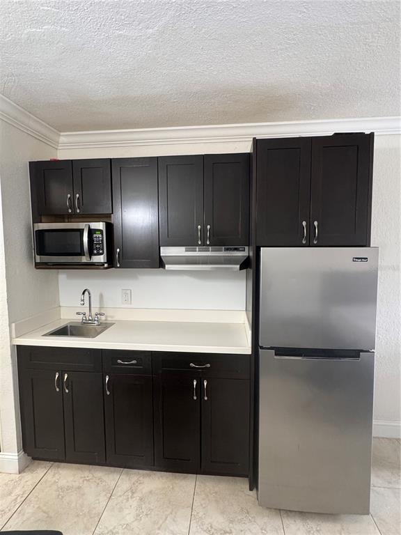 A small kitchen features dark wood cabinets, a stainless steel refrigerator, and a white countertop — 43420 HIGHWAY 27 UNIT 312, DAVENPORT, FL