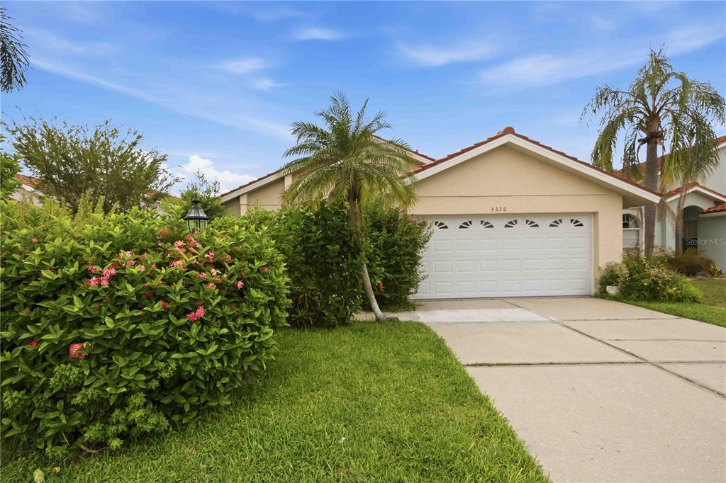 A tan house with a tiled roof is partially obscured by large, flowering green bushes — 4320 MARCOTT CIRCLE, SARASOTA, FL