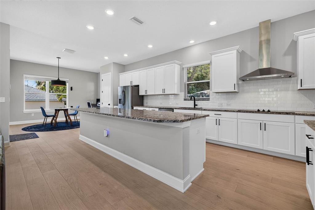 A modern kitchen features white cabinets, granite countertops, a large island, and light wood flooring — 293 18TH AVENUE S, ST PETERSBURG, FL