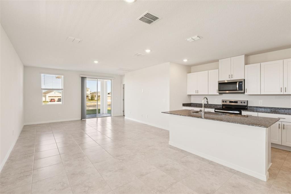 An open-concept kitchen and living area featuring white cabinets, granite countertops, and tile flooring — 879 SUNSHOWER DRIVE, LADY LAKE, FL