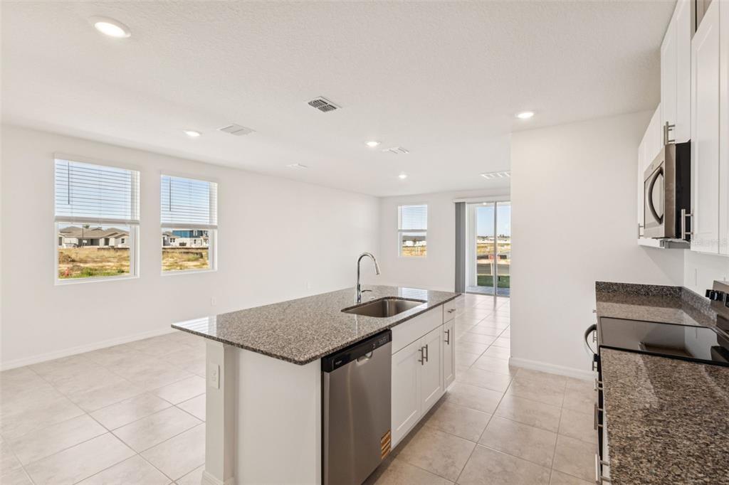 A kitchen with a granite island, stainless steel appliances, and white cabinets overlooks an open area — 879 SUNSHOWER DRIVE, LADY LAKE, FL