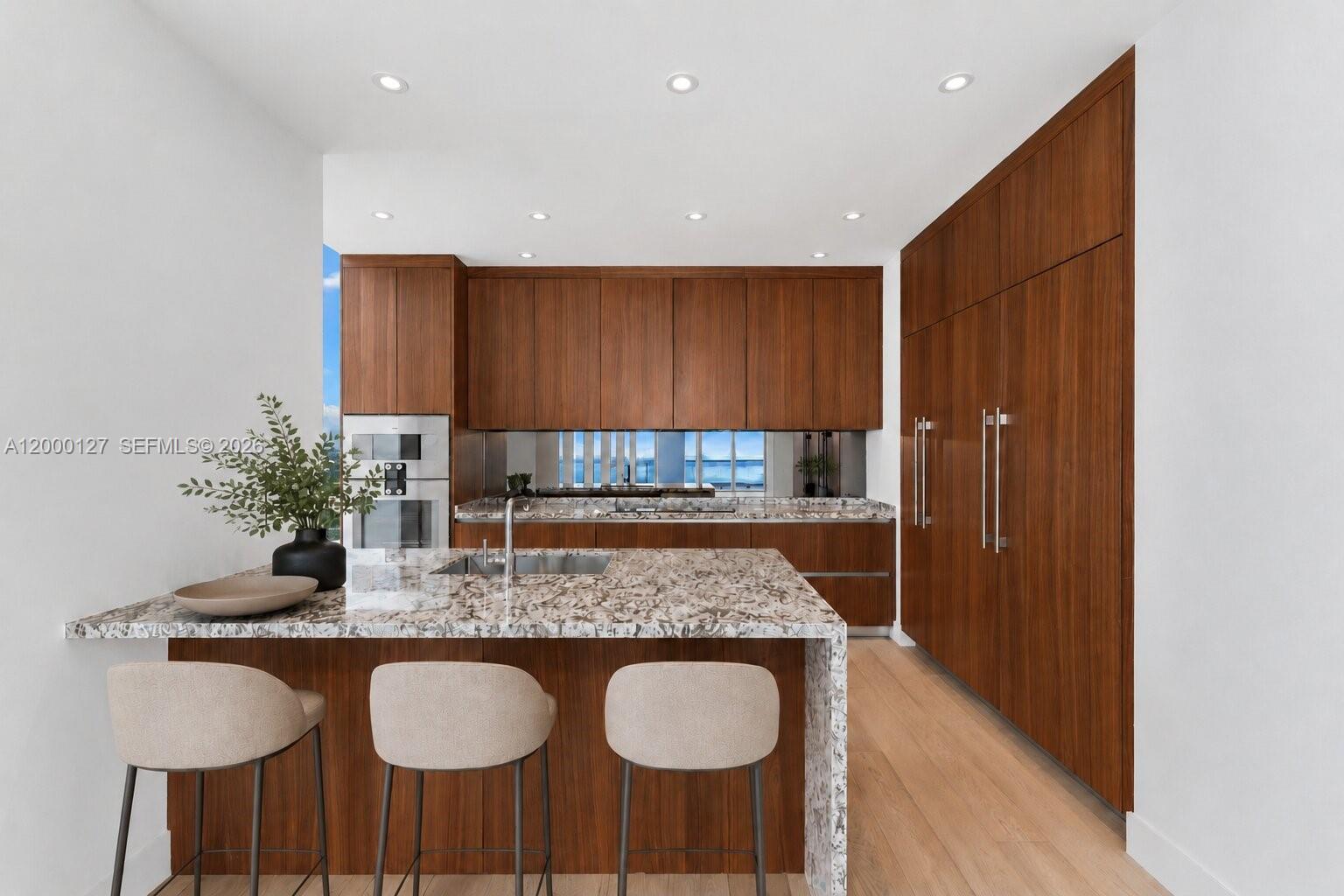 A modern kitchen features wood cabinetry, granite countertops, and floor-to-ceiling windows overlooking the ocean — 175 SE 25th Road # 3602, Miami FL 33129, MIAMI, FL