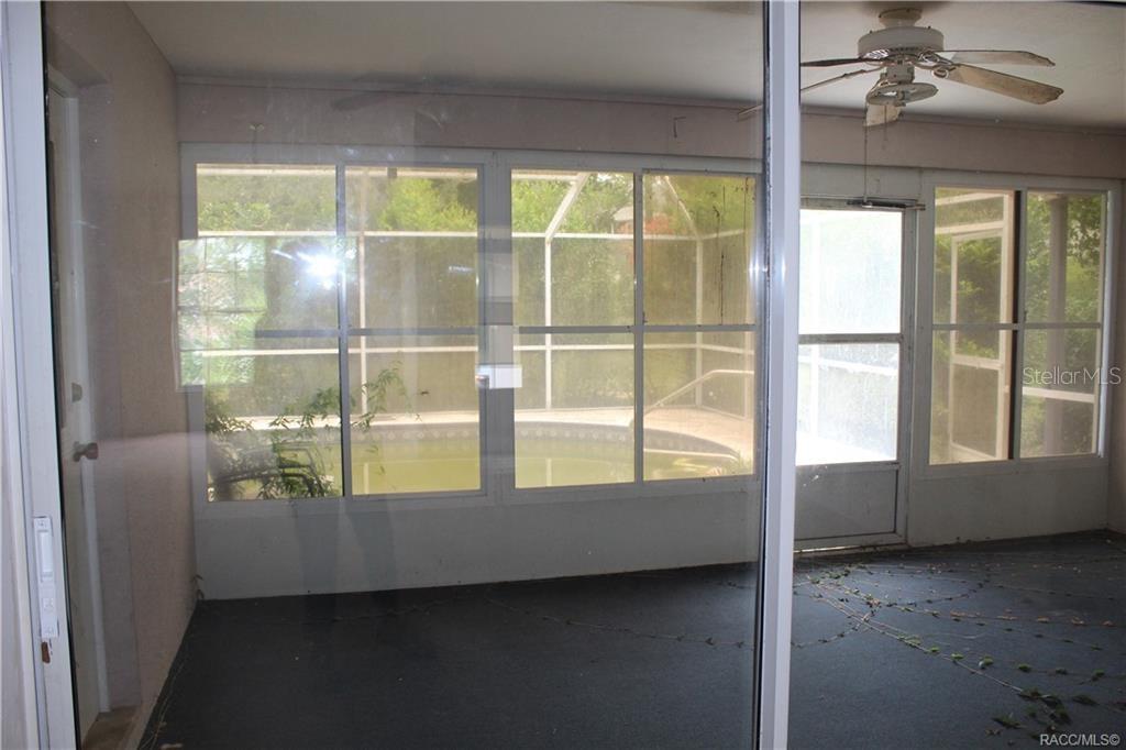 A view from inside a room looking out through glass doors at a screened pool enclosure — 742 W SUNSET STRIP DRIVE, BEVERLY HILLS, FL